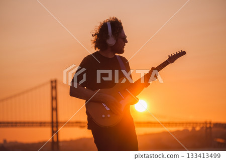 Hipster street musician in black playing electric guitar in street outdoors on sunset with lens flare and light leak Hipster street musician in black playing electric guitar in street outdoors on sunset with lens flare and light leak 133413499