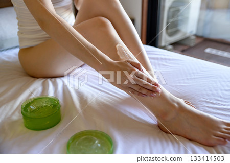 A young slender woman in underwear applying body gel to her legs in bed. Skin care, foot care, daytime color A young slender woman in underwear applying body gel to her legs in bed. Skin care, foot care, daytime color 133414503
