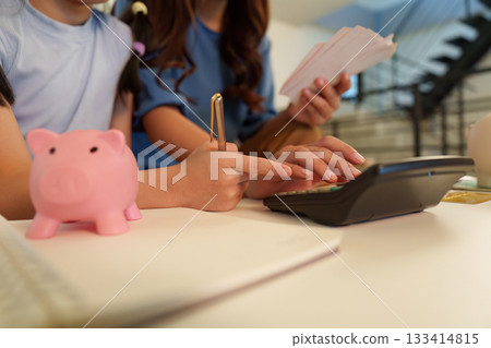 Learning Finance. Mother and daughter calculating savings with piggy banks. Learning Finance. Mother and daughter calculating savings with piggy banks. 133414815