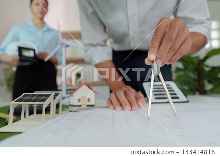 ESG Focused Design. Architect using compass on plans with sustainable models in foreground. 133414816