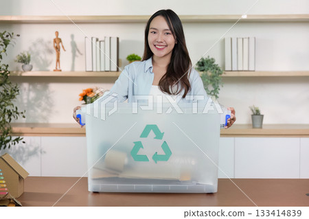 Recycling initiative. Woman smiling while holding a recycling box at home. Recycling initiative. Woman smiling while holding a recycling box at home. 133414839