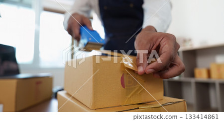 Packaging. Employee sealing boxes with tape in a delivery service environment. Packaging. Employee sealing boxes with tape in a delivery service environment. 133414861