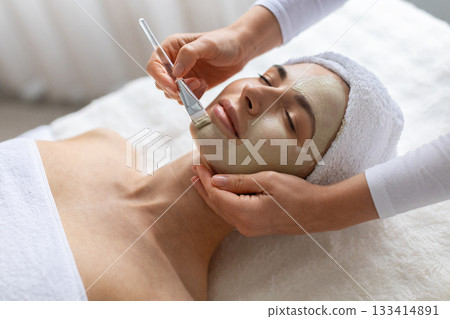 Young female receiving clay mask with focused brush strokes at spa Young female receiving clay mask with focused brush strokes at spa 133414891