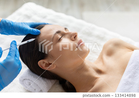 Young woman receiving a temple area injection during beauty procedure at spa 133414898