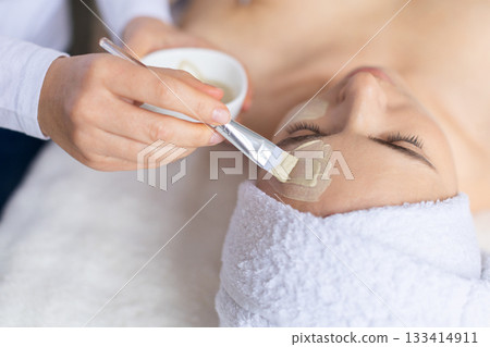 Young woman receiving precise clay mask application on her forehead Young woman receiving precise clay mask application on her forehead 133414911