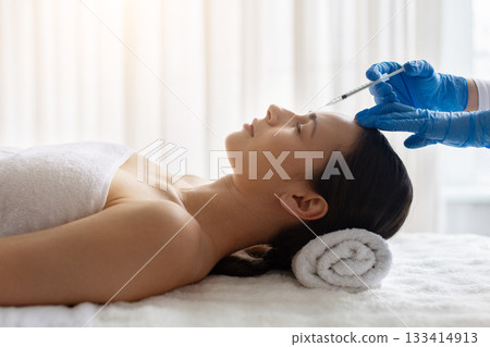 Beautician in gloves performing an aesthetic forehead injection to woman at spa 133414913