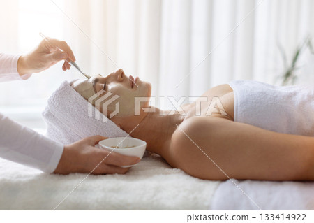 Beautician applying face clay mask to young beautiful woman at spa Beautician applying face clay mask to young beautiful woman at spa 133414922