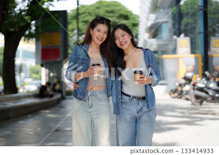 Casual Stroll. Two young women enjoying coffee and sharing smiles while walking together. Casual Stroll. Two young women enjoying coffee and sharing smiles while walking together. 133414933