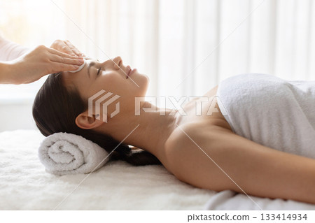 Young woman receiving gentle forehead cleansing at spa, enjoying skincare Young woman receiving gentle forehead cleansing at spa, enjoying skincare 133414934