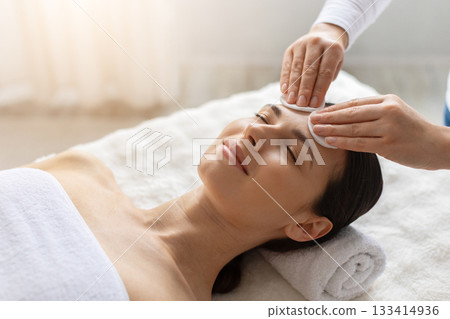 Therapist cleaning forehead of young woman with cotton pads during spa session Therapist cleaning forehead of young woman with cotton pads during spa session 133414936
