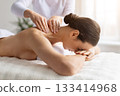 Relaxed young female lying face down at spa while receiving shoulder massage 133414968