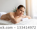 Smiling woman lying comfortably on massage bed with hands under chin 133414972