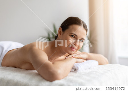 Smiling woman lying comfortably on massage bed with hands under chin 133414972
