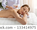 Young woman enjoying back massage while therapist applies exfoliating salt 133414975