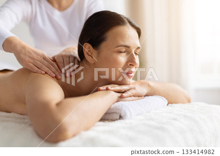 Female enjoying body massage at spa, eyes closed and resting on towel 133414982