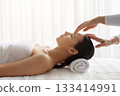 Young female relaxing during calming spa treatment as therapist gently touching forehead 133414991
