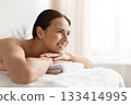 Smiling young woman lying on spa bed, resting her chin on towel 133414995