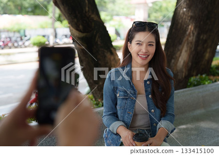 Capturing Smiles. A young woman poses for a photo while enjoying coffee outdoors. 133415100