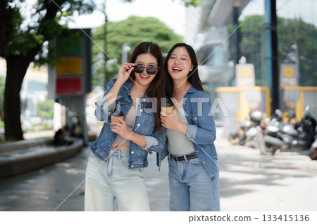 Friendship and Joy. Two young women enjoying coffee outdoors in casual denim outfits. 133415136