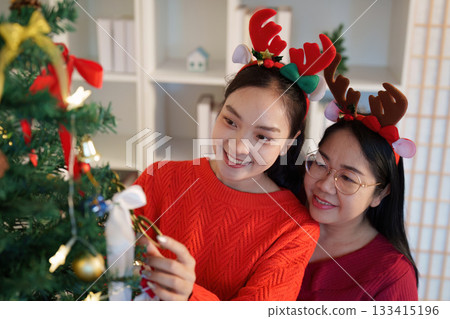 Festive Spirit. Women decorating Christmas tree with love and laughter. 133415196