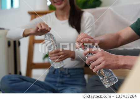 Sustainability. Young adults opening water bottles in a cozy living room. 133415264
