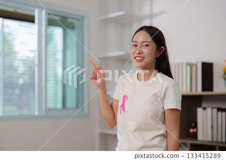 Empowerment. Young woman promoting breast cancer awareness with pink ribbon gesture. 133415289