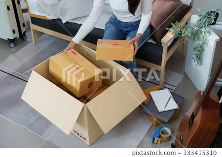 Woman organizing boxes in a cozy living room, reflecting on new adventures 133415310