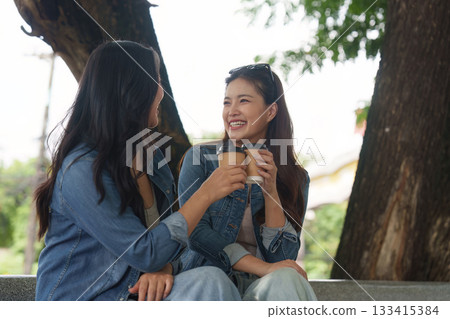 Coffee and Connection. Two young women enjoying coffee and laughter together in a park. 133415384