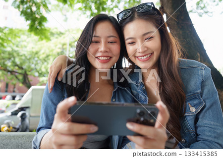 Friendship and Joy. Two young women sharing a delightful moment with coffee outdoors. 133415385