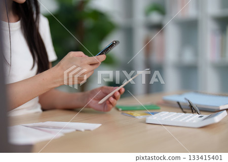 Smartphone Finance. Close-up of woman using phone to manage finances with receipts. Smartphone Finance. Close-up of woman using phone to manage finances with receipts. 133415401