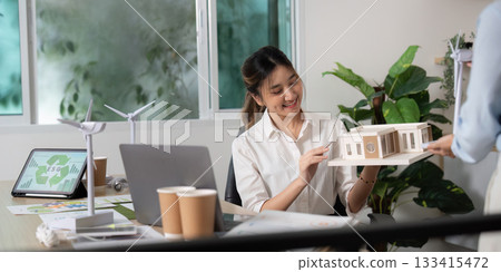 Sustainable Design. Businesswoman showcasing a model of an eco-friendly building. Sustainable Design. Businesswoman showcasing a model of an eco-friendly building. 133415472