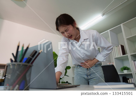 Young woman in office experiencing abdominal pain Young woman in office experiencing abdominal pain 133415501