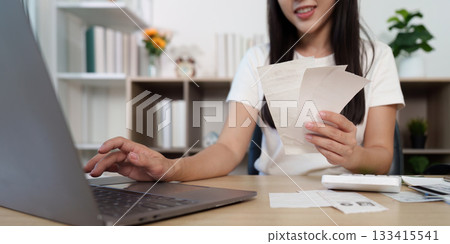 Efficient Financial Management. A woman organizing receipts while using a laptop. Efficient Financial Management. A woman organizing receipts while using a laptop. 133415541