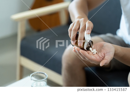 Medication Routine. Individual pouring pills from a bottle into hand at home. 133415587