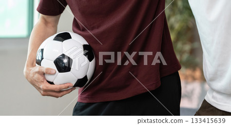 Soccer Enthusiasts. Two friends sharing a moment with a soccer ball indoors. 133415639