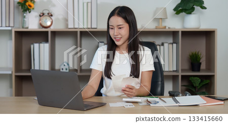 Positive Work Environment. A woman happily managing finances while using a laptop. 133415660