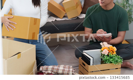 Couple Collaborating to Unpack Boxes in Cozy Living Room Couple Collaborating to Unpack Boxes in Cozy Living Room 133415685
