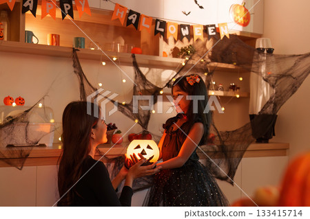 Halloween Joy. Mother and daughter sharing a glowing pumpkin moment. Halloween Joy. Mother and daughter sharing a glowing pumpkin moment. 133415714
