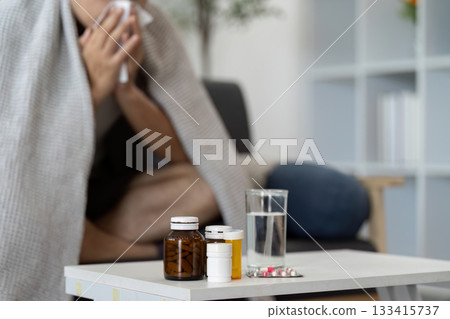 Home Care. Individual feeling unwell, surrounded by medication and water. 133415737