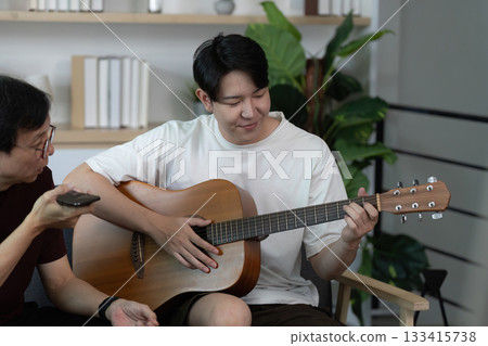 Guitar Lesson. A young man learning guitar from a friend in a cozy setting. Guitar Lesson. A young man learning guitar from a friend in a cozy setting. 133415738