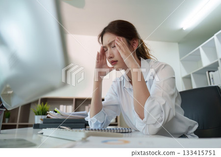 Mental Strain. Young woman holding her head in pain at her office desk. Mental Strain. Young woman holding her head in pain at her office desk. 133415751
