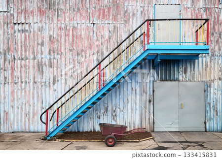 Wall of an old industrial building with stairs and a wheelbarrow. 133415831
