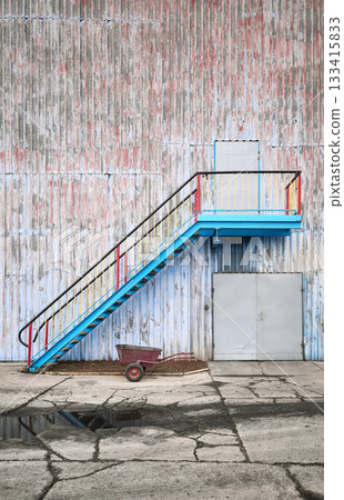 Wall of an old industrial building with stairs and a wheelbarrow. 133415833