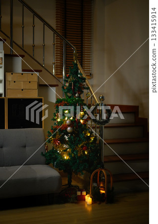 Cozy Christmas Tree with Glowing Lights in living room Interior with grey Sofa and Staircase Beside Cozy Christmas Tree with Glowing Lights in living room Interior with grey Sofa and Staircase Beside 133415914