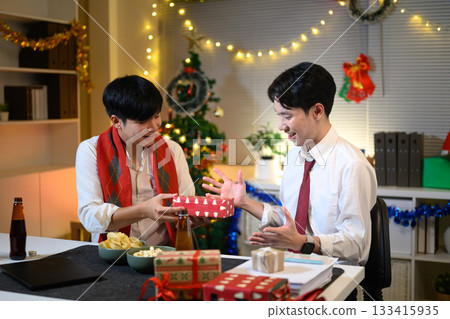 Office employees exchanging presents at work, feeling festive in office with Christmas tree and decorations. 133415935