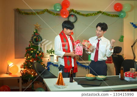 Office employees exchanging presents at work, feeling festive in office with Christmas tree and decorations. 133415990