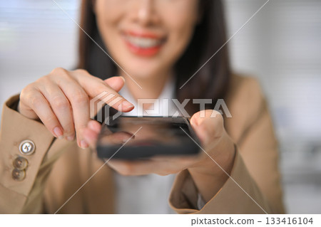 Close-up of businesswoman using smartphone, tapping screen with focus and smile Close-up of businesswoman using smartphone, tapping screen with focus and smile 133416104