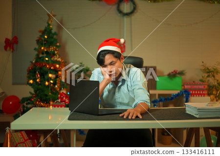 Bored, Christmas hat and portrait of a tired man in the office with a laptop, exhausted and young businessman with xmas decorations in the modern workplace. Bored, Christmas hat and portrait of a tired man in the office with a laptop, exhausted and young businessman with xmas decorations in the modern workplace. 133416111