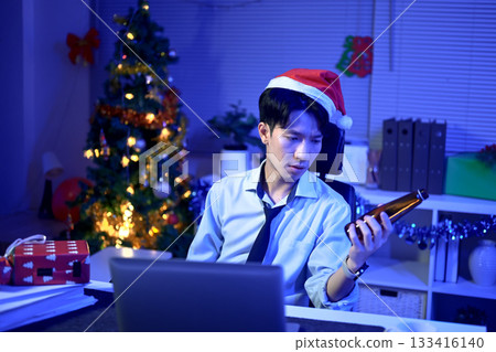 lonely corporate employee in Santa hat drinking beer at New Year midnight in office. Overtime work running out of time on crisis, Festive loneliness concept 133416140