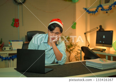 Bored, Christmas hat and portrait of a tired man in the office with a laptop, exhausted and young businessman with xmas decorations in the modern workplace. 133416167